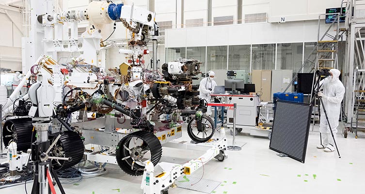 The rover being built in the lab as people in white overalls work on it.