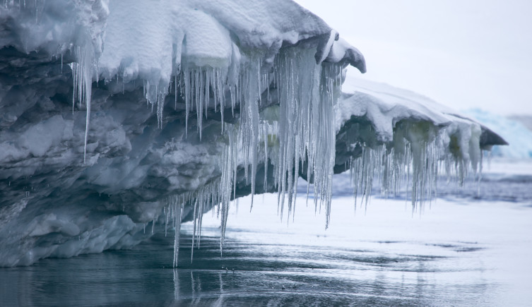 A melting iceberg floats on the sea, with icicles hanging off it.