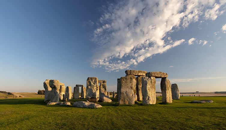 Stonehenge sits in the foreground, tinged orange-pink with the setting sun. 