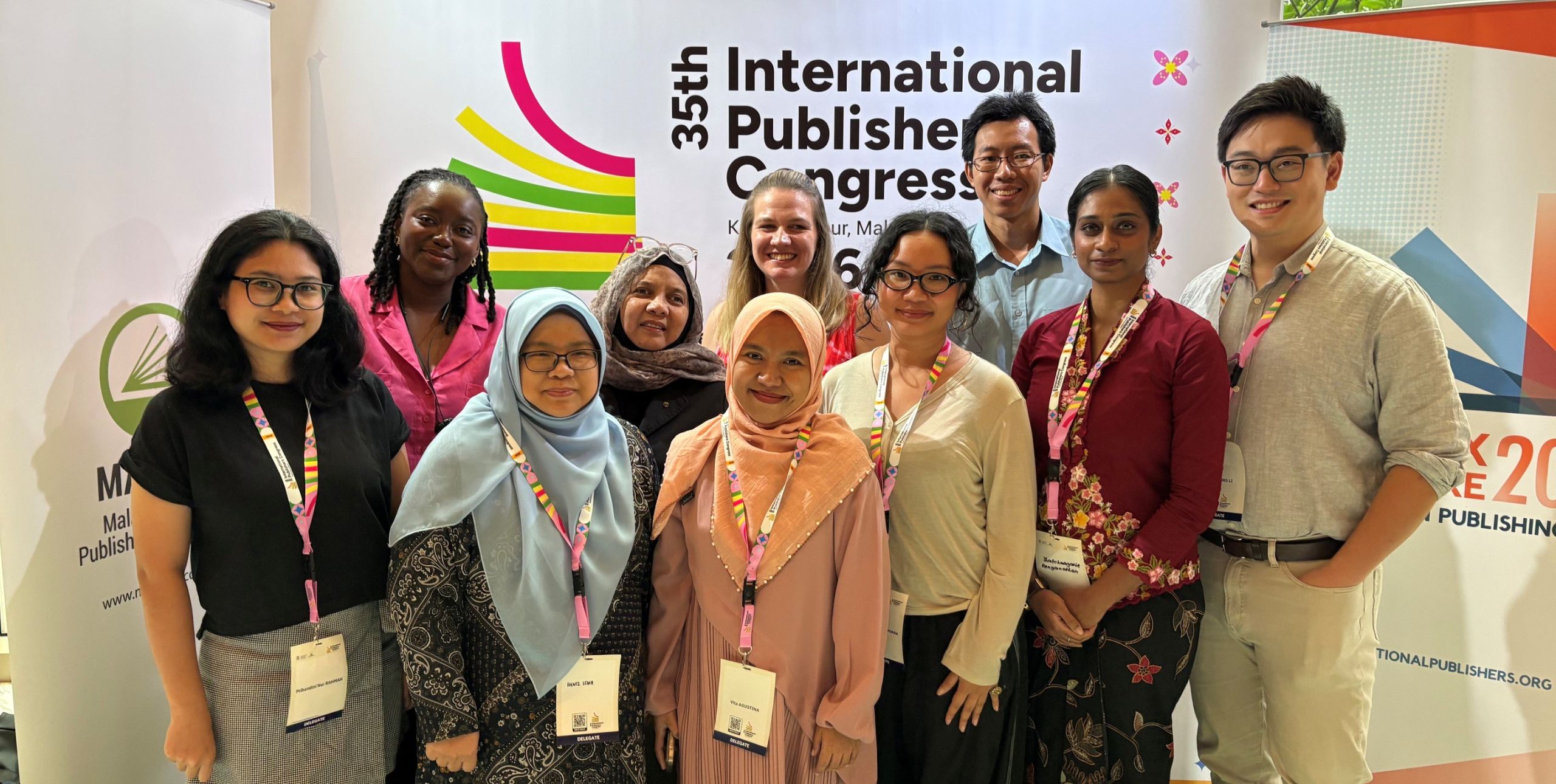 A diverse group of 10 people smiling at the camera in front of a conference backdrop