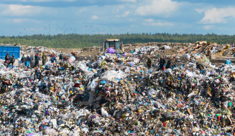 A bulldozer drives through a pile of plastic waste at a landfill site