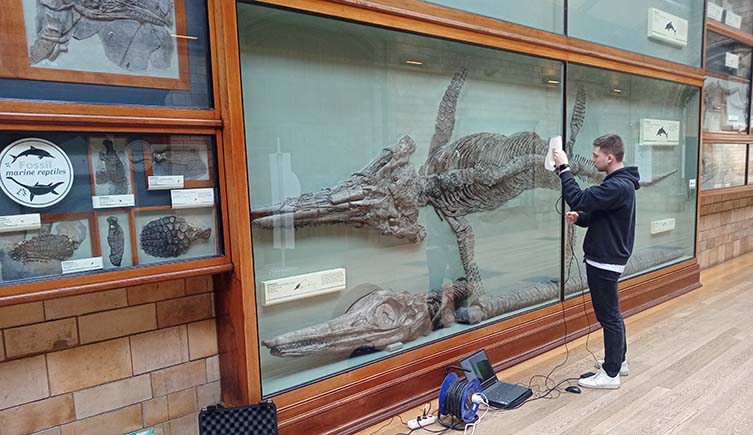 Antoine Laboury scans a ichthyosaur mounted on the wall behind glass.
