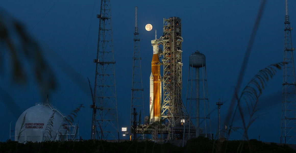 The SLS on the launch pad at dusk, with the moon in the background. 