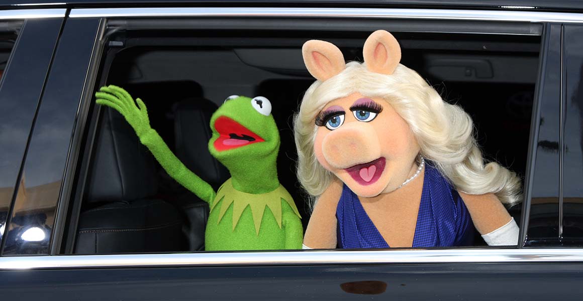 Kermit the Frog and Miss Piggy wave from the window of a car.