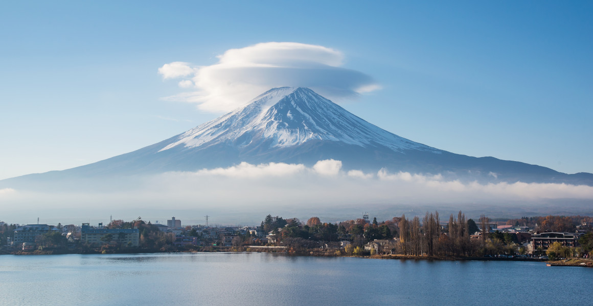 A cloud sits over the top of Mt Fuji, rising above a lake.