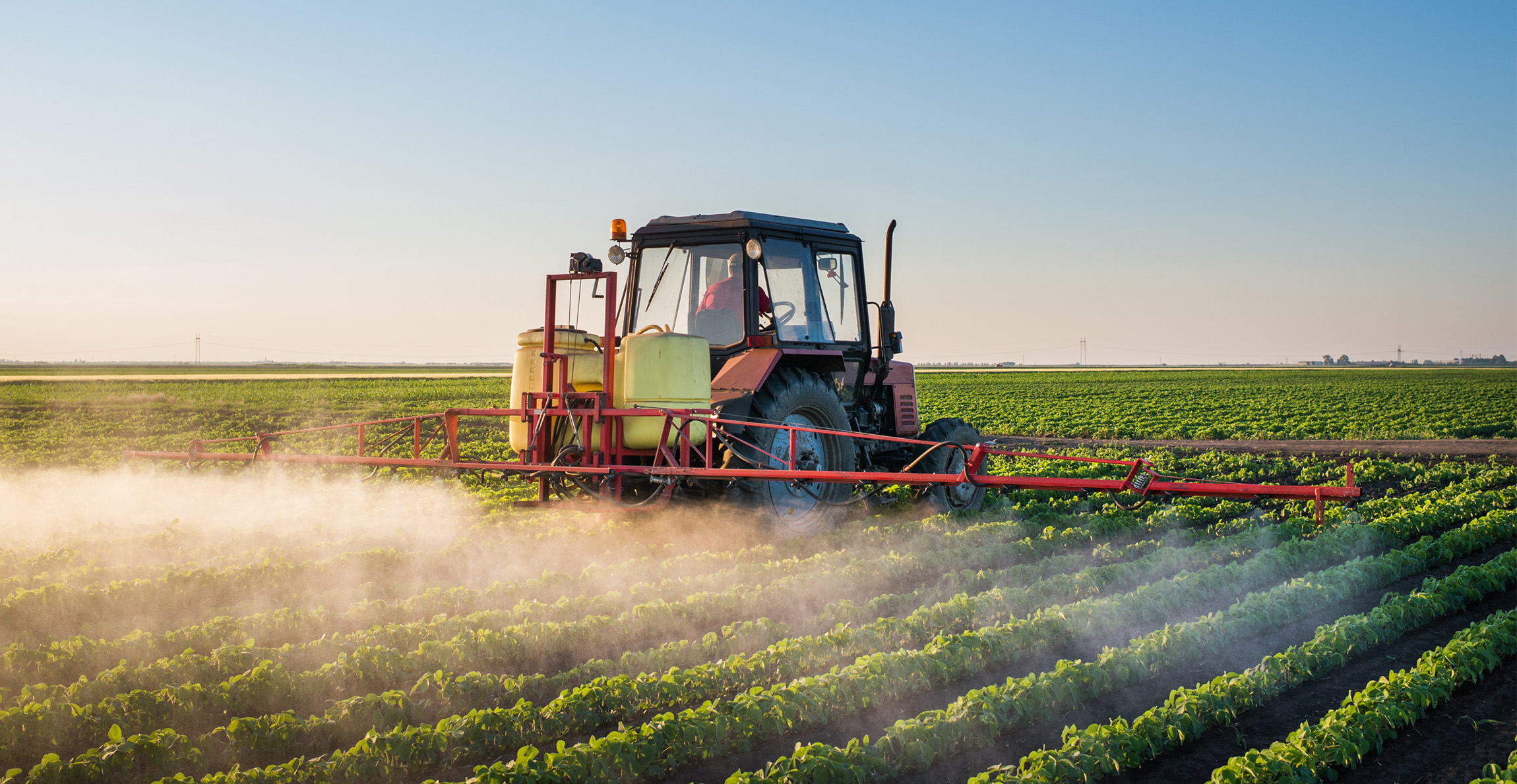 A tractor moves through a field spreading pesticide
