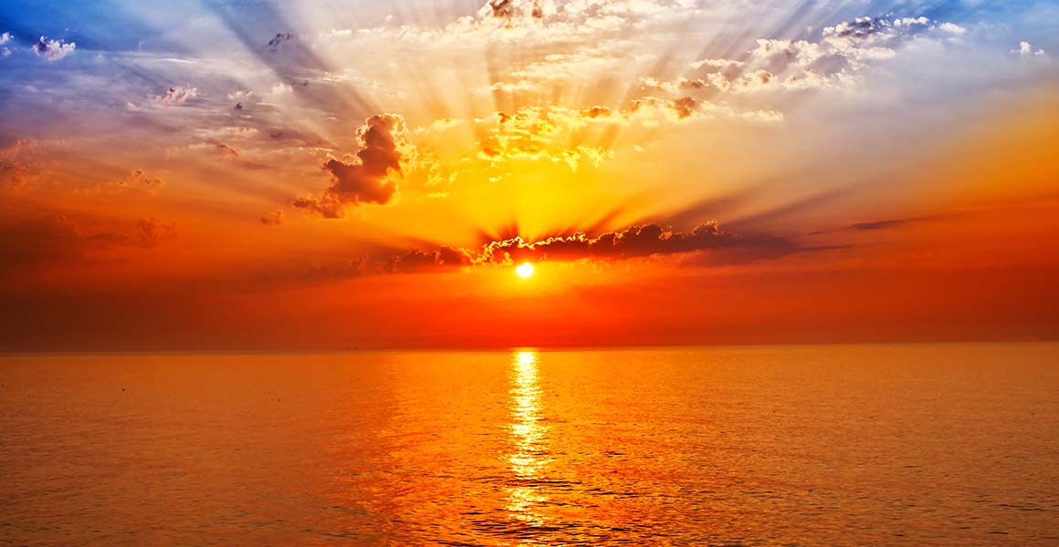 An orange sky with low sun over the ocean.