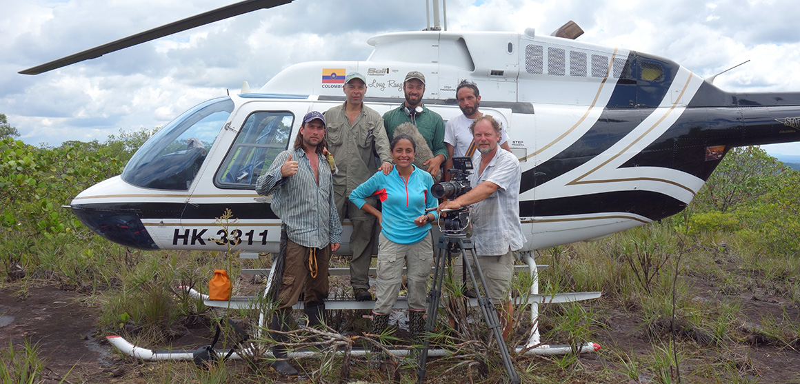 Dr Blanca Huertas and her team of five people stand with a video camera on a tripod in front of the helicopter that delivered them to the national park. They’re surrounded by shrubs and other low-growing plants.
