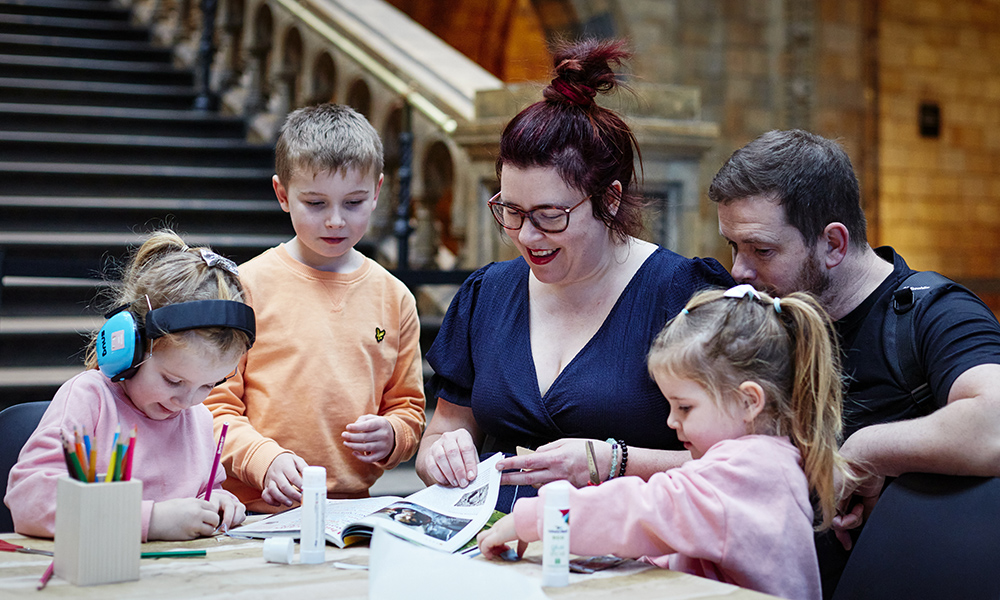 Three children draw on a table as a man and a woman help them