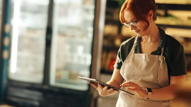 Happy supermarket owner using a digital tablet while standing in her grocery store.