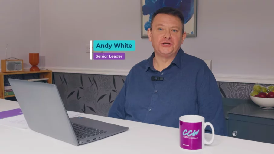 Andy White, Senior Leader. He is sitting with his laptop at the dining table in the home wearing a blue button down shirt.