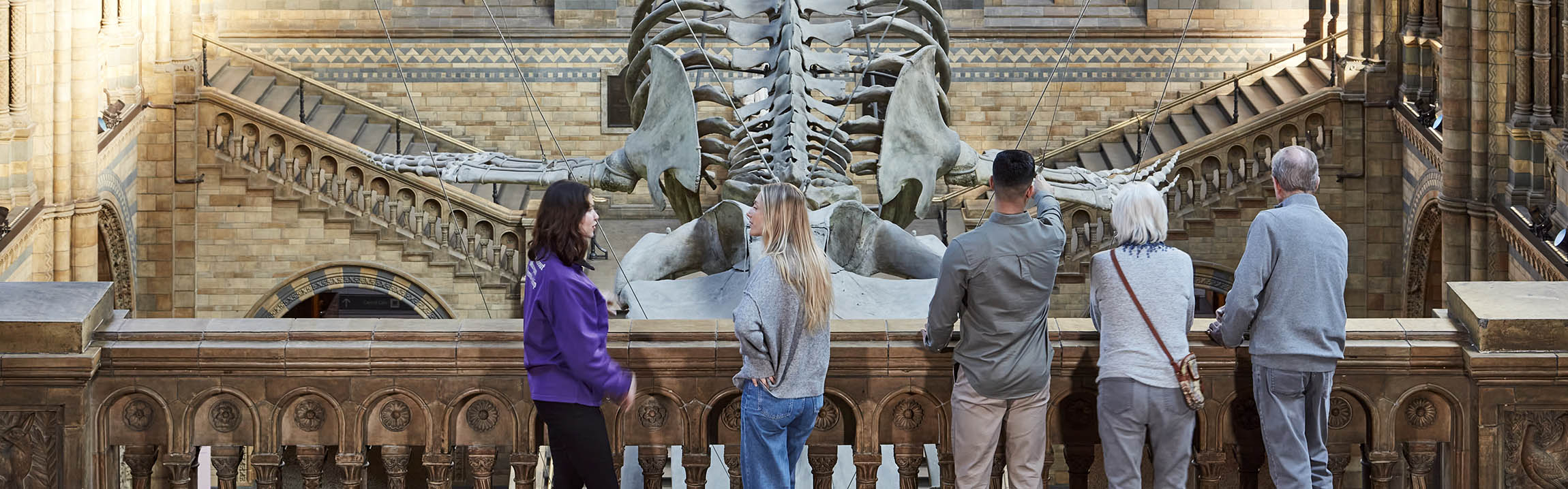 A tour guide talks to a group of people on a balcony at Hintze Hall overlooking Hope the blue whale