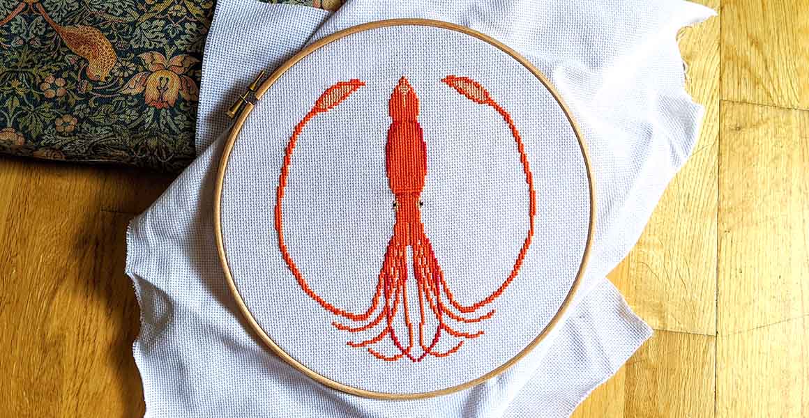 The completed cross-stitch of the giant squid showing it holding its two tentacles to circle around the squids body.