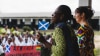 Two ladies, on Ghanaian and one Scottish address students at an outdoor assembly in Ghana