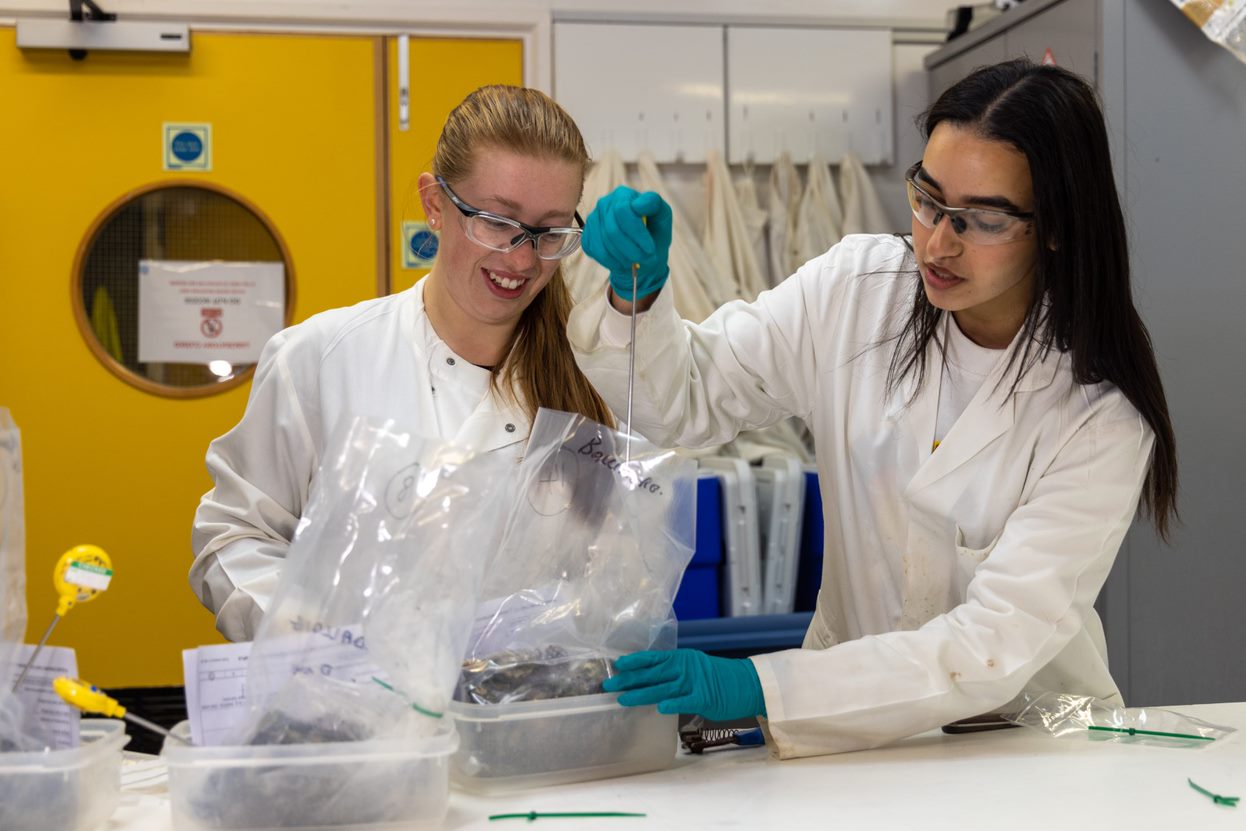 Two people in lab coats and gloves