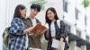 Three young people, two women and one man, standing outside looking at an open book.
