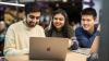 Three students sitting next to each other looking at a laptop.