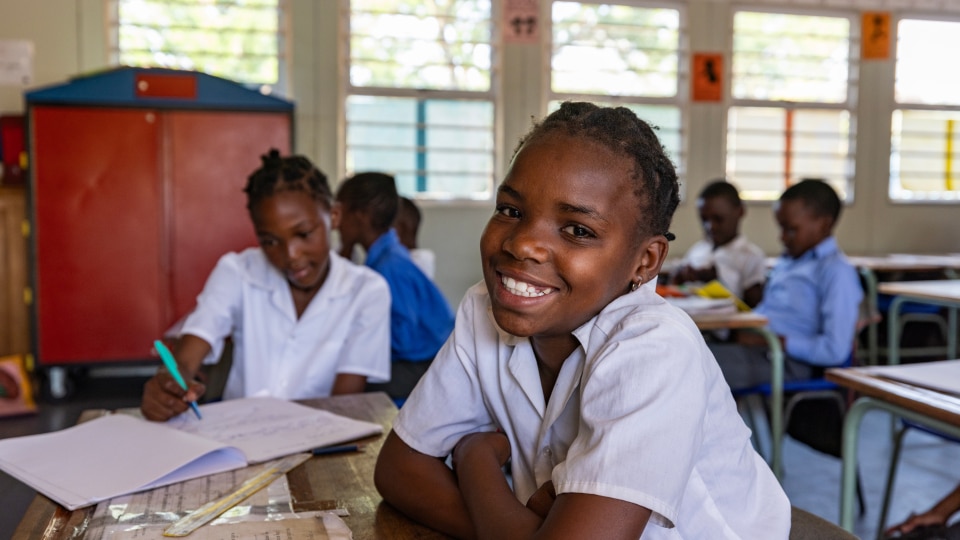Black secondary aged learner in a classroom, smiling at the camera. 