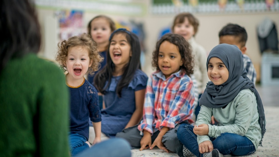 children sitting on the floor, listening to a teacher, also sitting