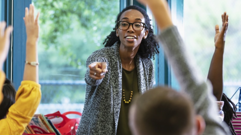A teacher selecting a learner among a group of children with raised hands
