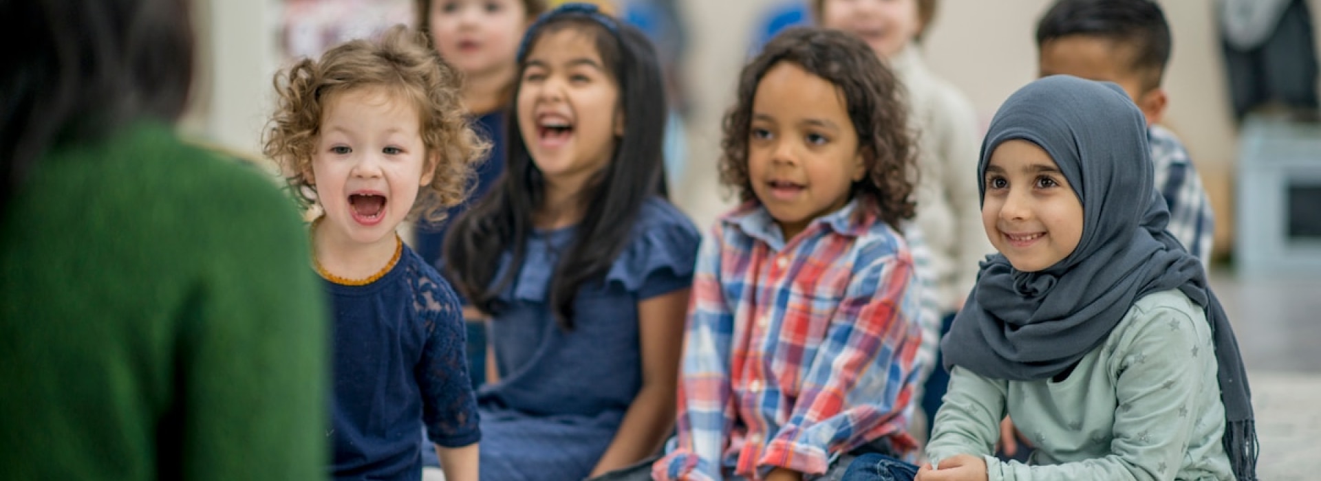 children sitting on the floor, listening to a teacher, also sitting