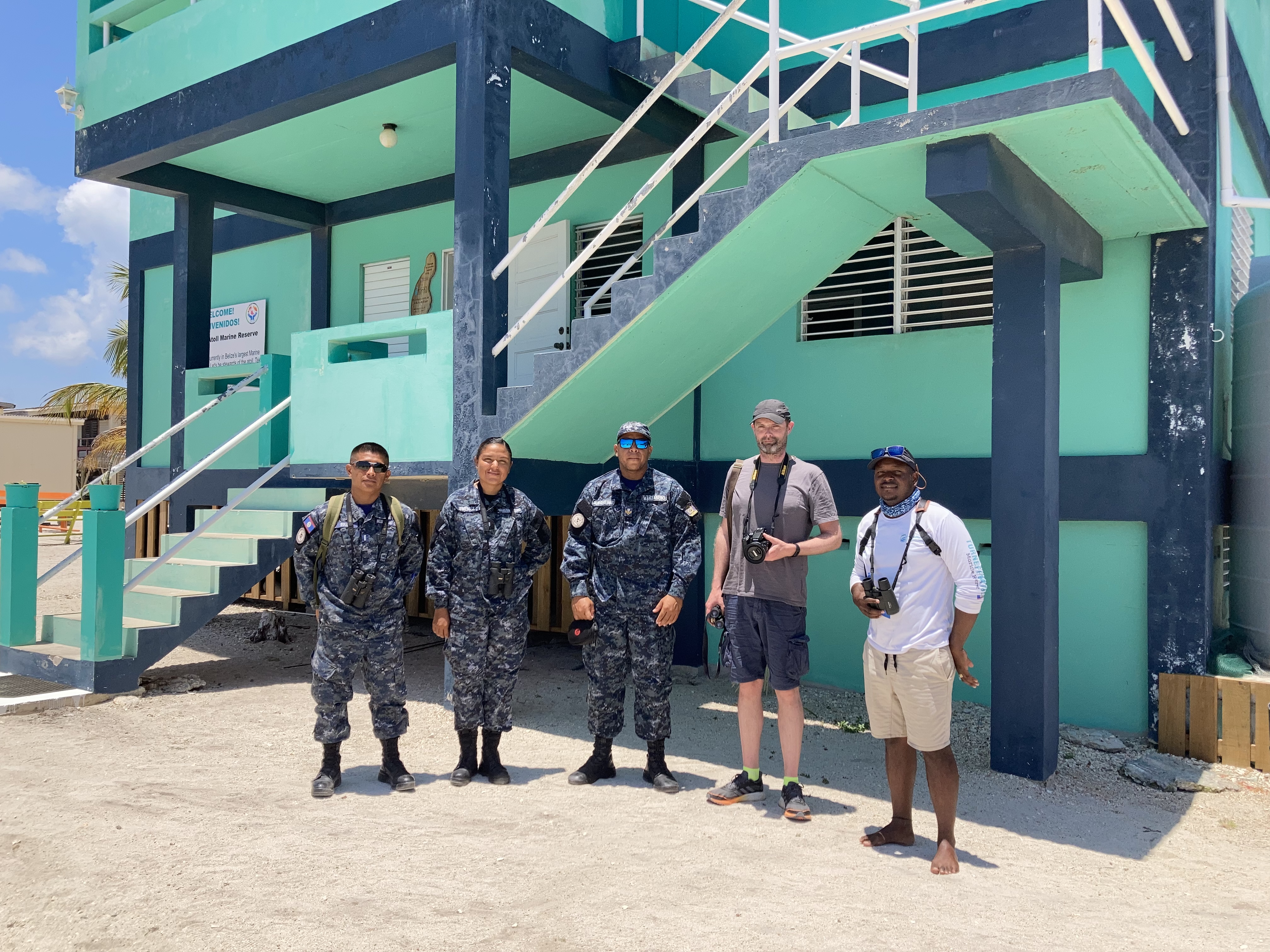 Belize enforcement staff standing in a line in uniform with two people standing next to them in shorts