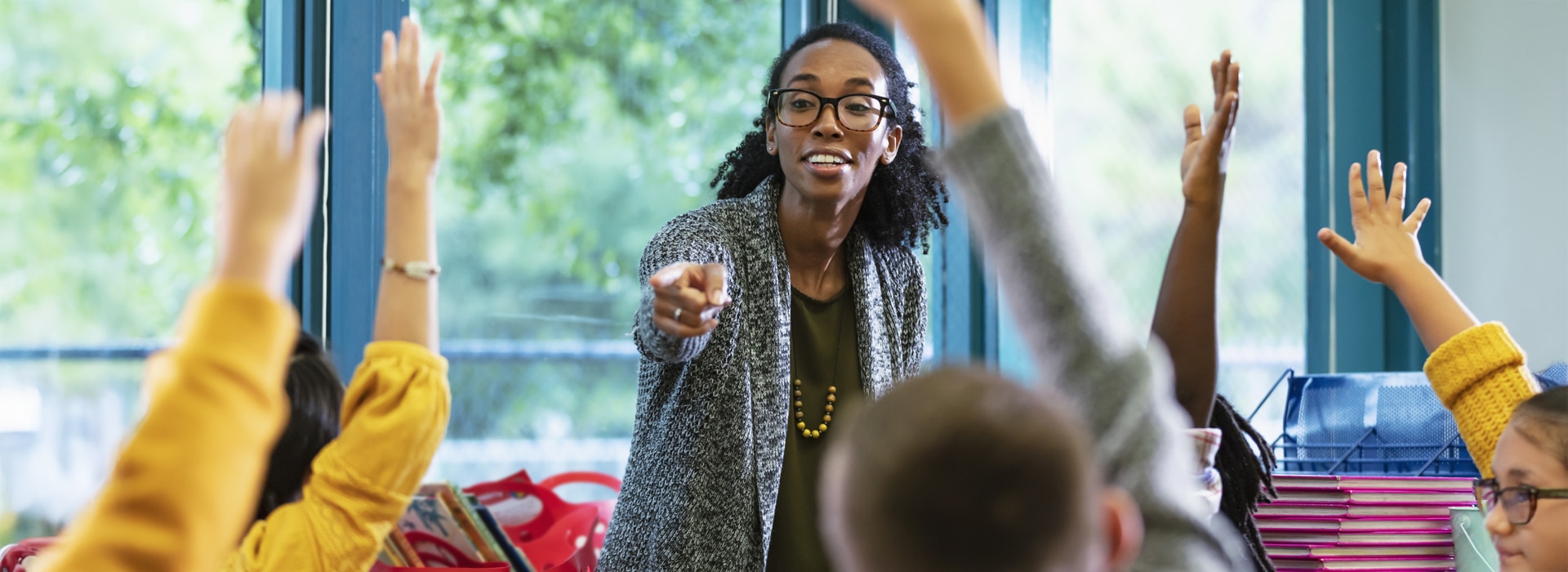 A teacher selecting a learner among a group of children with raised hands