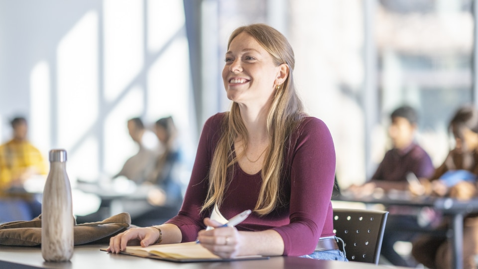smiling young woman writing at a desk in a classroom
