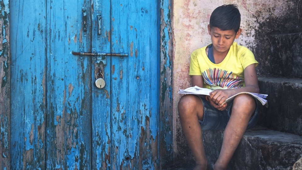 A young male learner sitting on outdoor steps, reading an exercise book