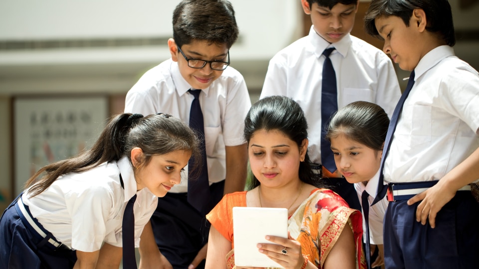 South Asian teacher looking at a tablet with a group of learners standing round her