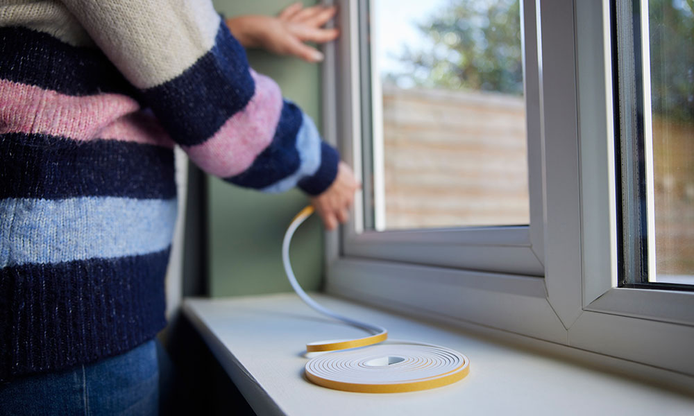 A person applying adhesive foam strips to a window to exclude draughts