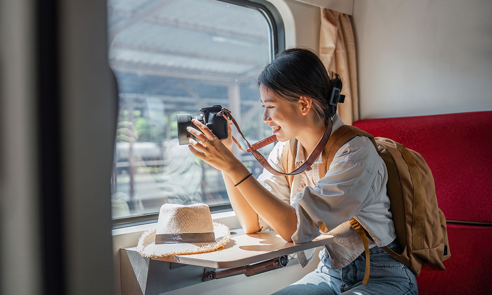 A young woman travelling on a train and taking a photo of the view from the window