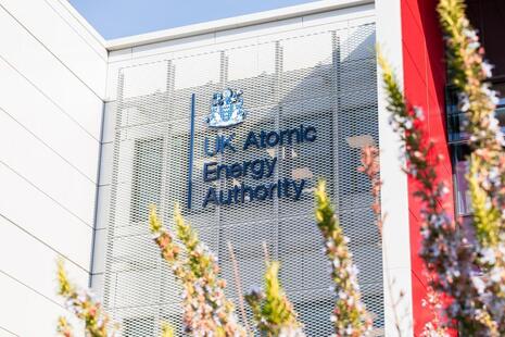 The UK Atomic Energy Authority crest and logo on the side of its facility through trees in blossom.