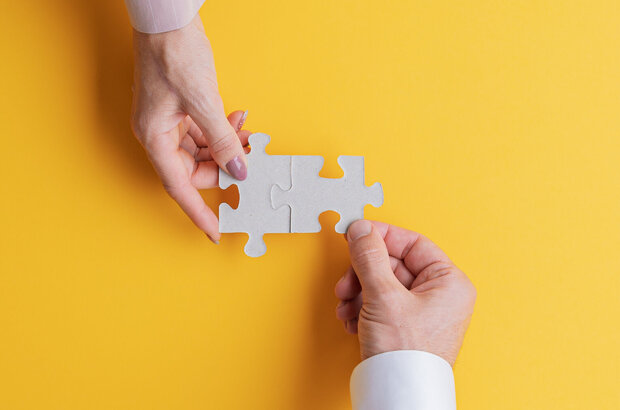 Male hand and female hand joining two matching jigsaw pieces together.