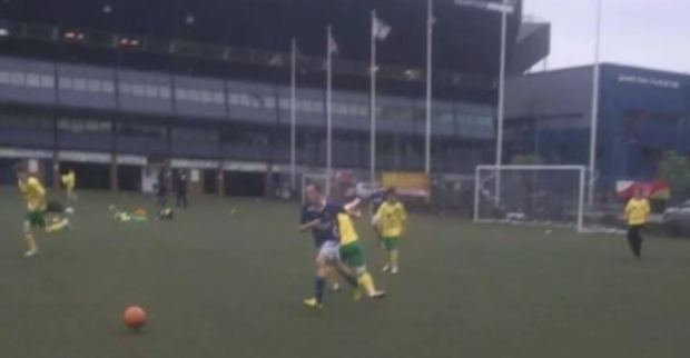 An action shot image of Harry in a blue shirt in the centre of the image chasing an orange football on a football field.