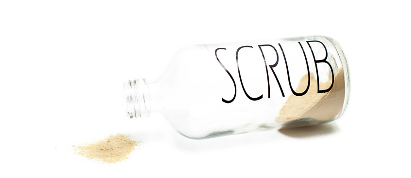 Glass botle with a yellow powder scrub on a white background