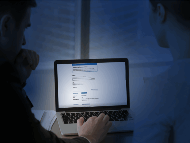 An image of two people looking at a laptop screen, showing a gov.uk page.