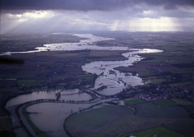 Image shows an aerial view of the Lower Derwent Valley Nature reserve. Grey clouds loom overhead and a bursting river flows at the bottom of the valley
