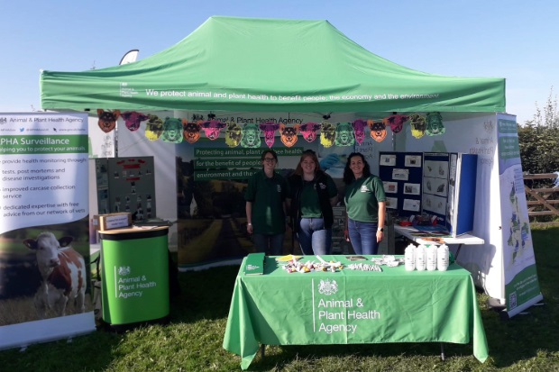 Image of three APHA members of staff standing in an APHA gazebo on grass