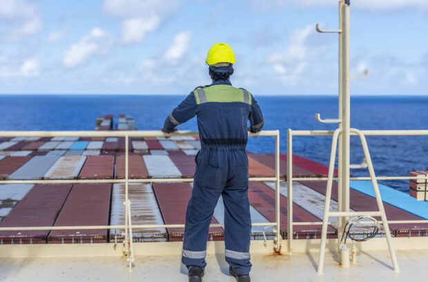 Sailor in overalls with back turned looking out to sea from deck of a cargo vessel