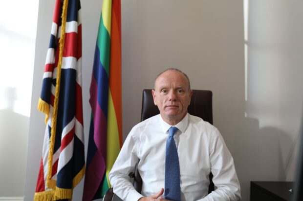 Landscape photo of Mike Freer in front of Union Jack and LGBT flag