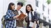 Three young people, two women and one man, standing outside looking at an open book.
