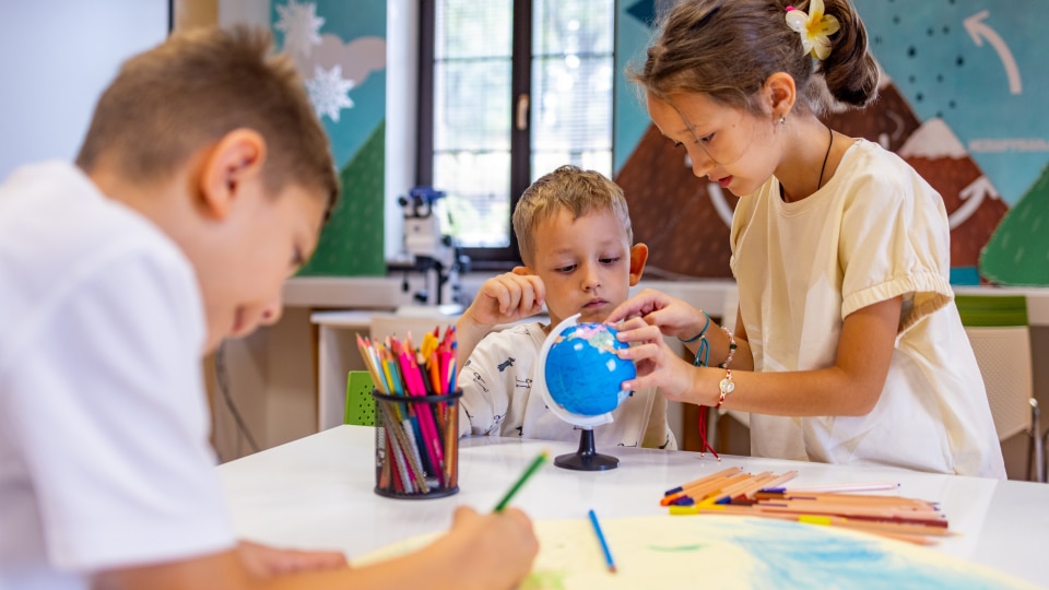 Two children looking at a small globe in the classroom and one boy colouring a poster