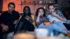 Group of people sitting together on a sofa watching TV.