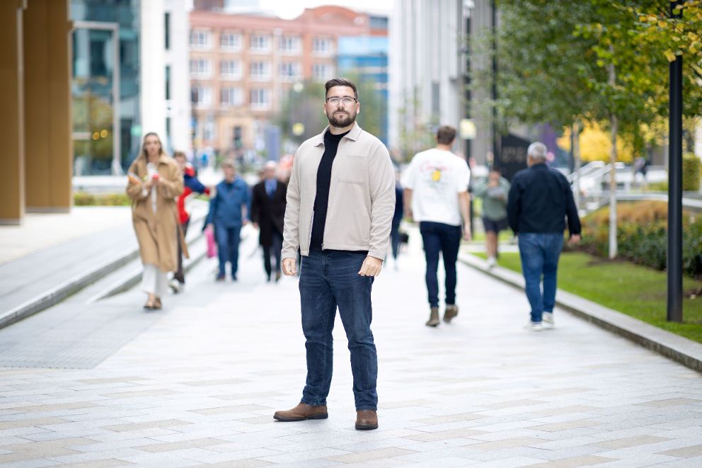 Dan Taylor standing outside NHS England offices with people walking in the street in the background.
