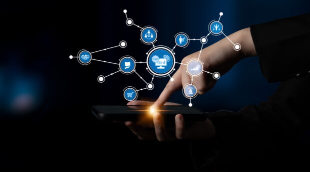 A hand interacting with a smartphone displaying various interconnected icons, representing the digital transformation and innovative technology across different sectors.
