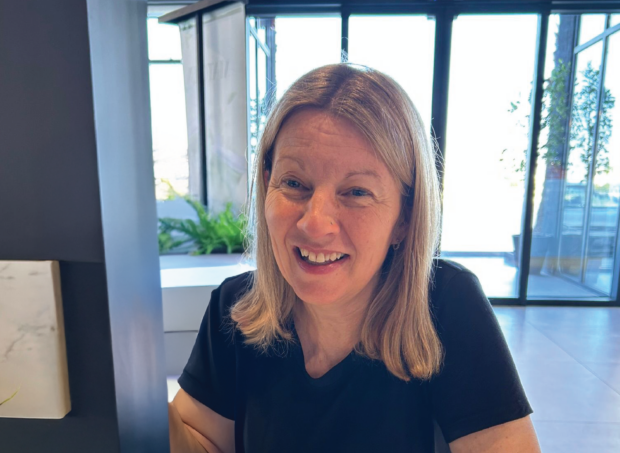 Image of Justine, smiling. Justine has shoulder length blonde hair and is wearing a black t-shirt.