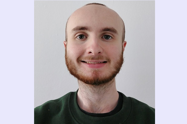 A man with ginger beard and short hair at the sides, wearing a green jumper.
