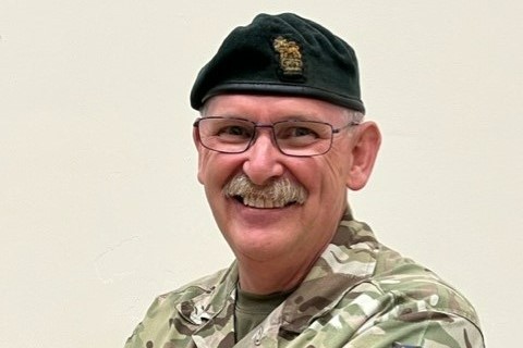 A man wearing an Army uniform and beret smiles to the camera