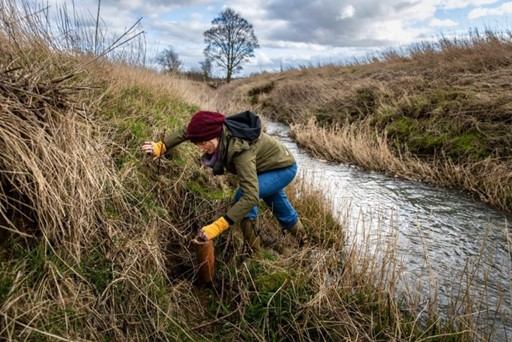 Volunteer in wellies and winter outdoor gear on the bank of a river, climbing away from the river.